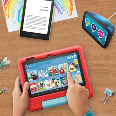 A kid playing on a Amazon Fire 7 kids tablet with other Amazon kids devices lying on the table.
